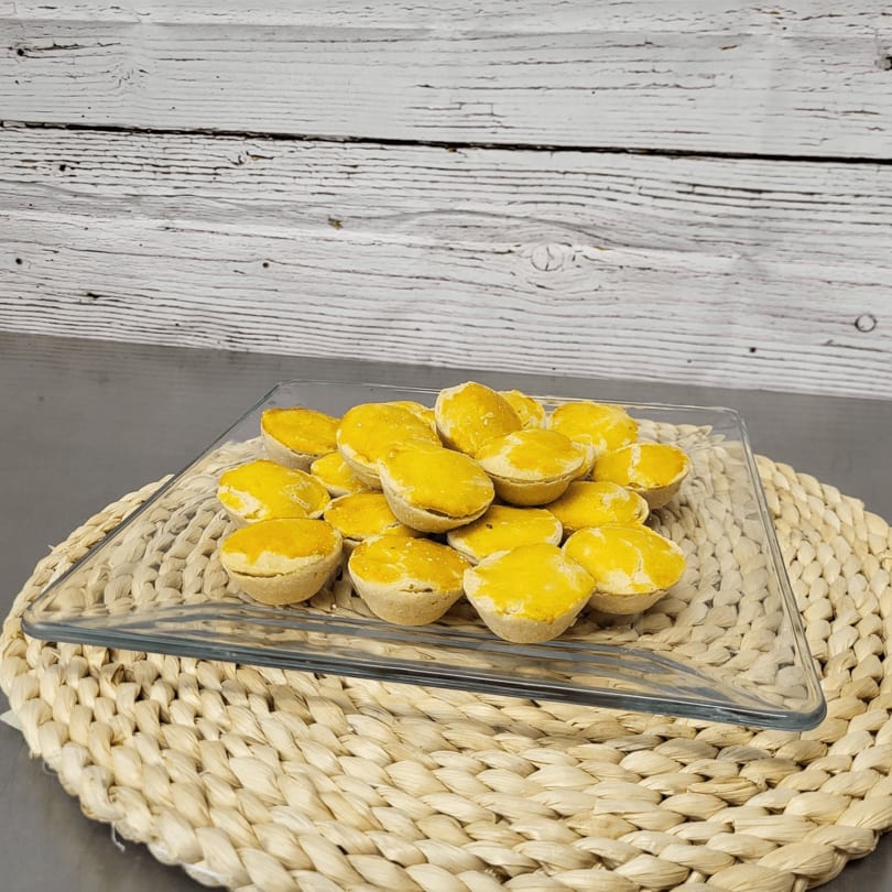 A clear glass platter filled with small, golden-topped pastries sits on a woven placemat.
