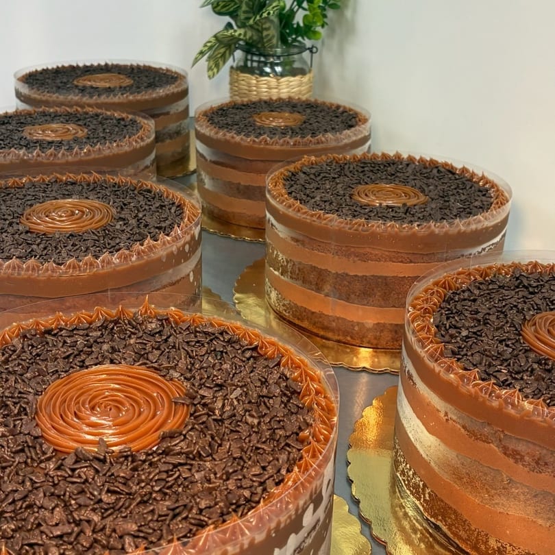 Multiple round chocolate cakes with caramel swirls and chocolate sprinkles in clear containers.