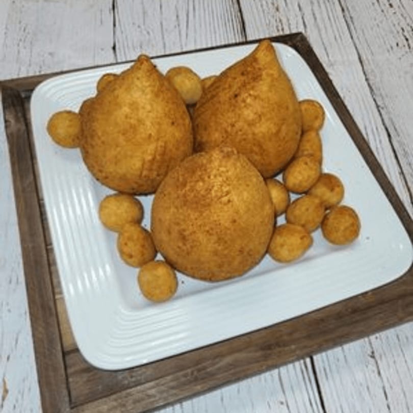 Three large and many small golden-brown coxinha on a white rectangular plate with a wooden tray.
