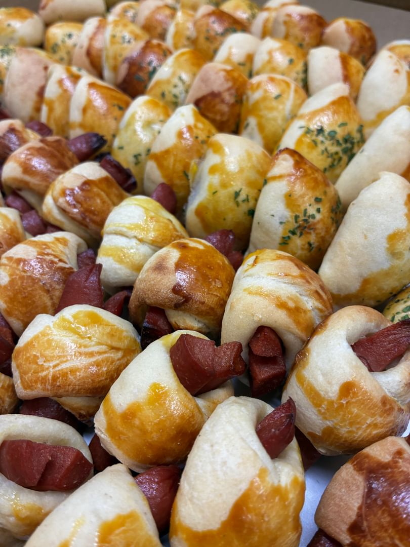 Close-up of many golden-brown pigs in a blanket, some with visible sausage and herb sprinkles.